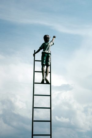 A child standing at the stop of a stair and reaching for the sky